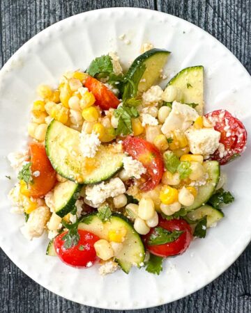 white plate with a zucchini corn and tomato salad